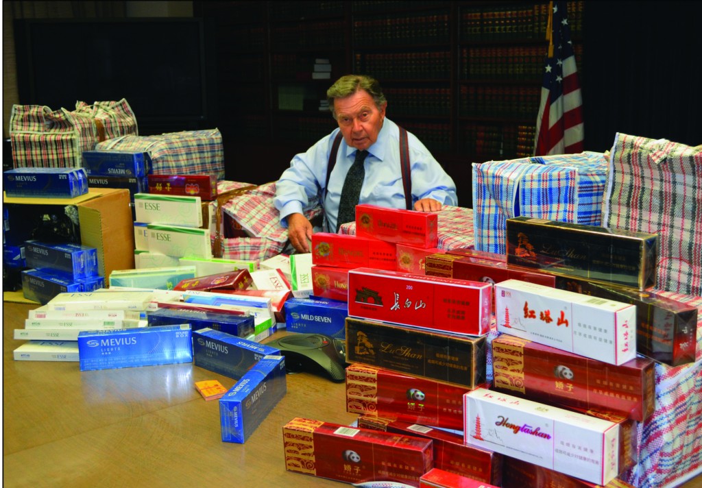 Queens District Attorney Brown sits among the approximately 1,151 boxes of illegal American and Asian cigarettes, which were allegedly seized during an investigation of illegal cigarette trafficking in Queens.  Photo Courtesy of District Attorney's Office