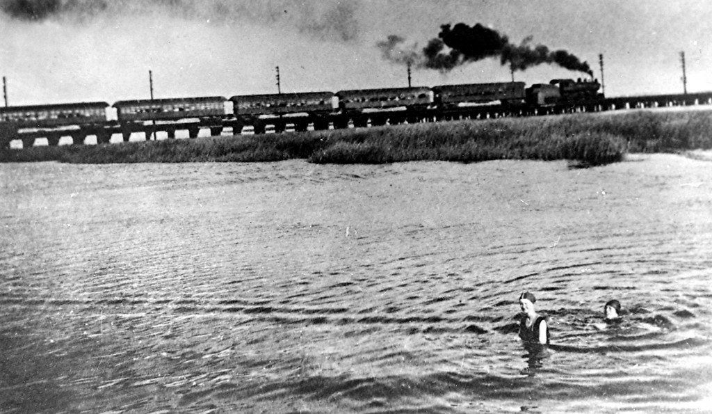 Just off Broad Channel, a Long Island Rail Road train heads towards Rockaway while two women go for a swim. Powered then by a coal burning locomotive, it crosses Jamaica Bay along the same route the A subway train takes today. The photo is from 1914.  Photo courtesy of The Queens Borough Public Library, Long Island Division, Rugen Photos.