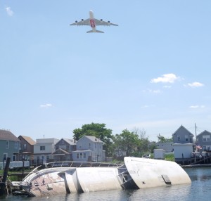 A low-flying plane takes off from JFK Airport above a boat sinking into Hawtree Creek. Construction at the airport has caused many planes to fly over Howard Beach at low altitudes, which has led residents to complain about the increased noise. Forum Photo by Greg Zwiers
